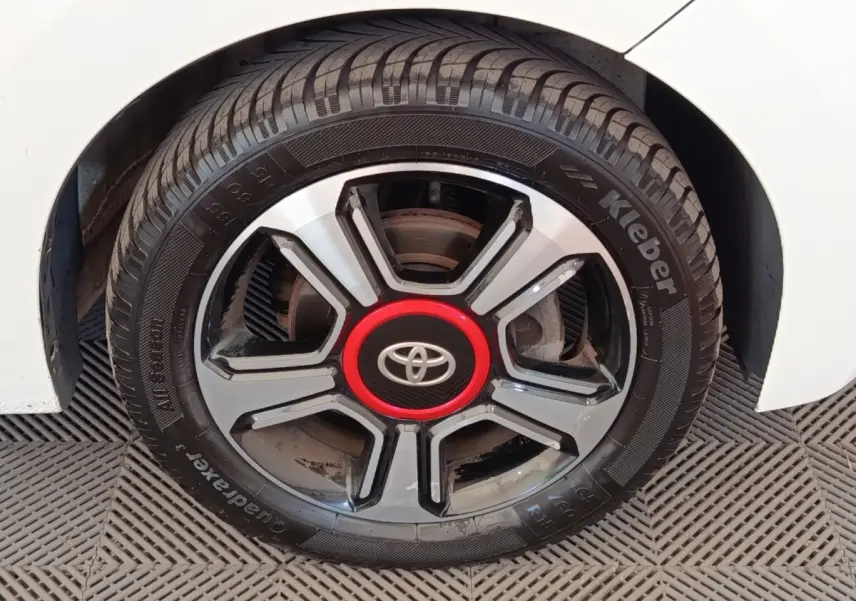 Gros plan sur la roue avant droite d'une Toyota Aygo blanche, jante noire et argent avec logo Toyota rouge au centre.