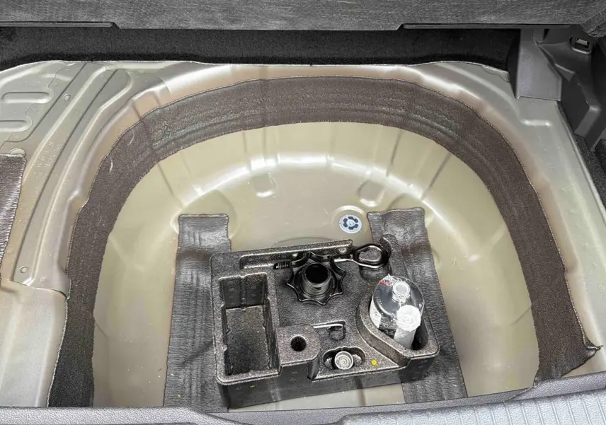 Vue plongeante sur le coffre ouvert d'un Volkswagen T-Cross gris, montrant le rangement sous la moquette.