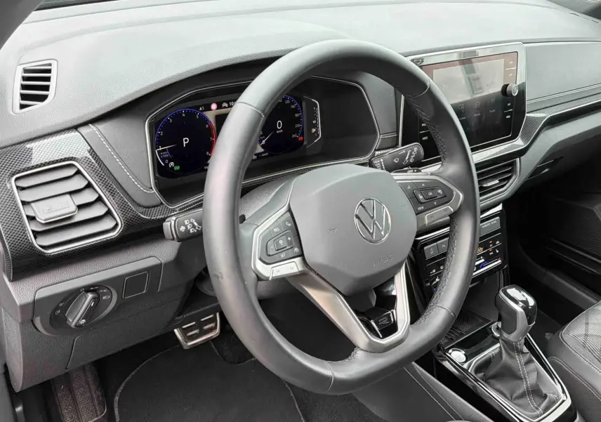 Vue intérieure du volant cuir et tableau de bord digital du Volkswagen T-Cross 2025 avec boîte manuelle, finition gris et détails noirs.