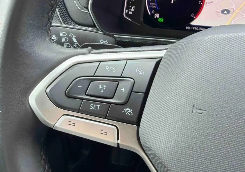 Gros plan sur les commandes à gauche du volant cuir du Volkswagen T-Cross 2025, avec affichage digital en arrière-plan.