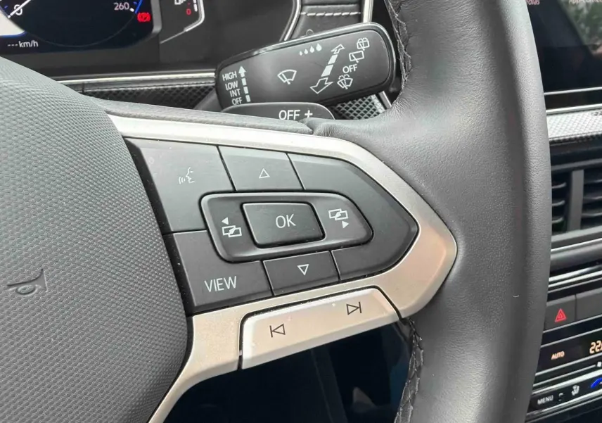 Gros plan sur les commandes multifonctions en cuir du volant du Volkswagen T-Cross, intérieur gris et tableau de bord numérique.