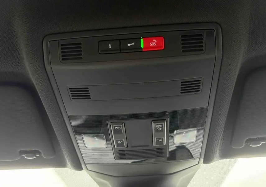 Vue en contre-plongée du panneau de commandes de toit intérieur du Volkswagen T-Cross gris, avec boutons SOS et éclairage.