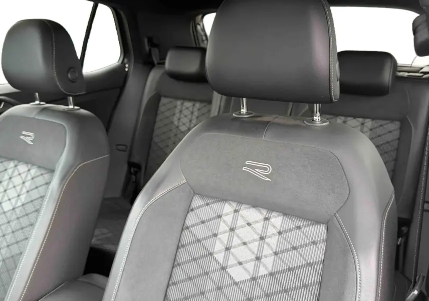 Gros plan sur les sièges avant gris du Volkswagen T-Cross avec surpiqûres blanches et logo R brodé.