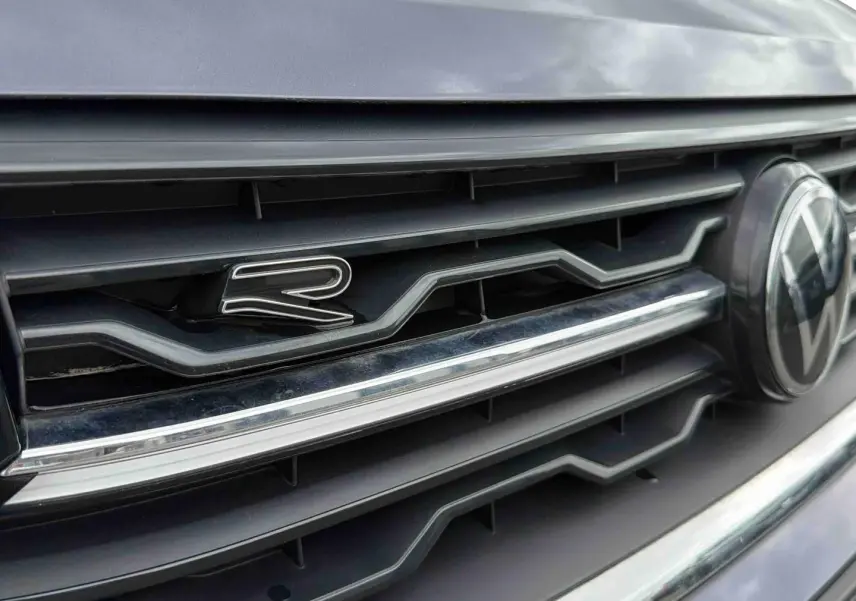Gros plan sur la calandre grise du Volkswagen T-Cross avec logo VW et badge "R" distinctif.