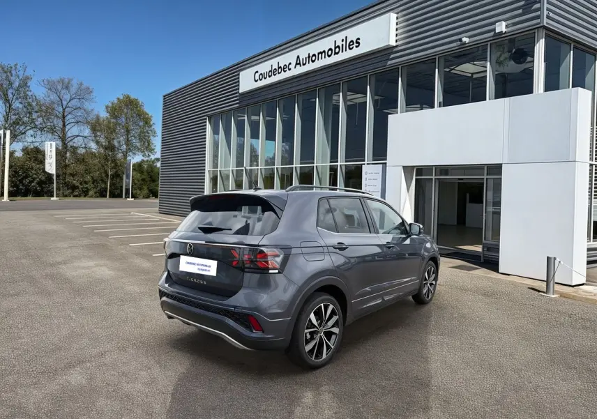 Volkswagen T-Cross gris en 3/4 arrière droit, avec jantes alliage et pare-chocs R-Line, devant un concessionnaire.