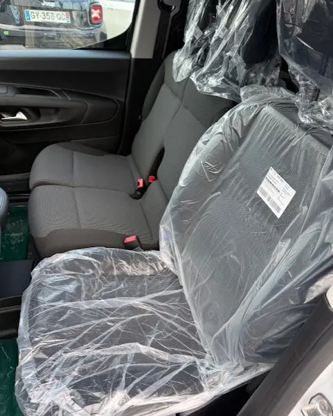 Vue intérieure côté droit du Citroën Berlingo 2026, sièges avant en tissu gris protégés par des housses plastiques.