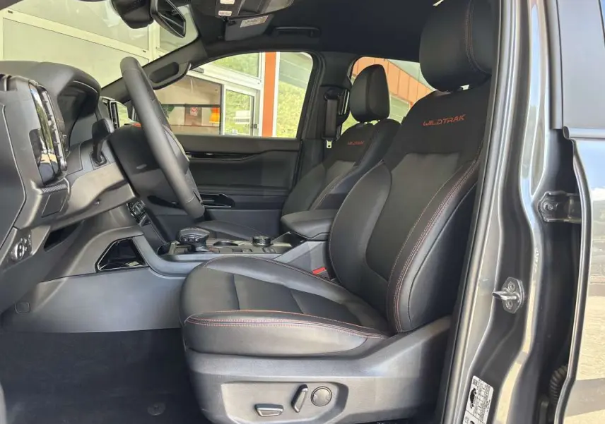Vue intérieure côté conducteur du Ford Ranger Wildtrak gris carbone, sièges cuir noirs avec surpiqûres orange et logo Wildtrak brodé.