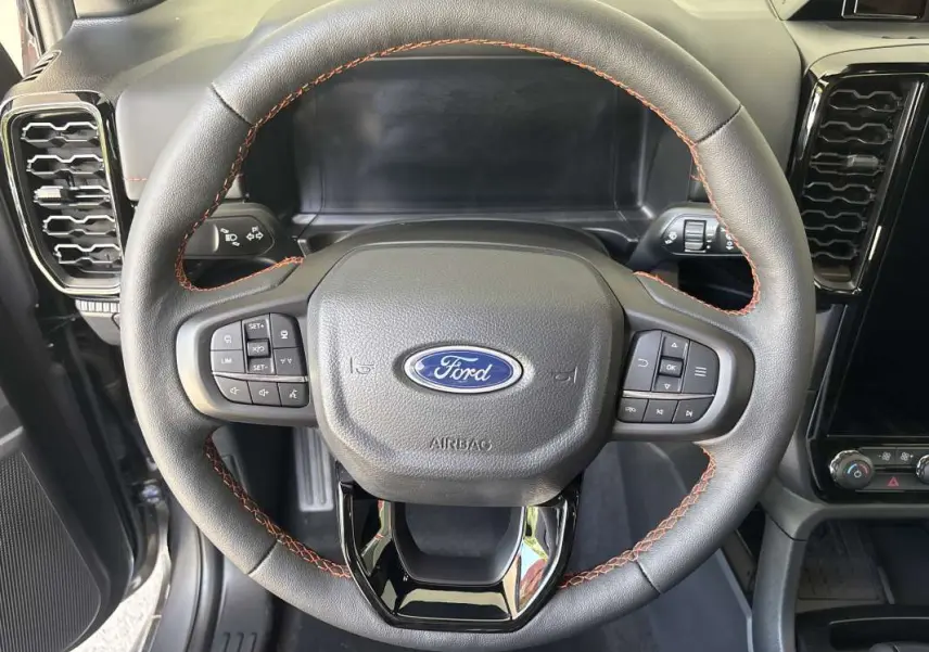 Vue rapprochée du volant cuir noir avec surpiqûres marron du Ford Ranger Wildtrak Plus 2026, tableau de bord en arrière-plan.