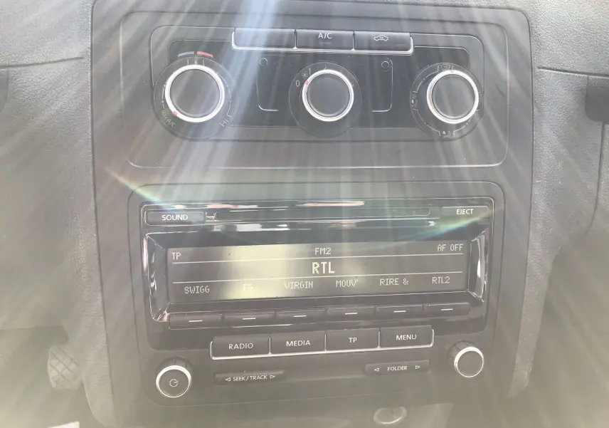 Gros plan sur la console centrale noire du Volkswagen Caddy Maxi Van blanc, affichant la radio sur RTL et les commandes de climatisation.