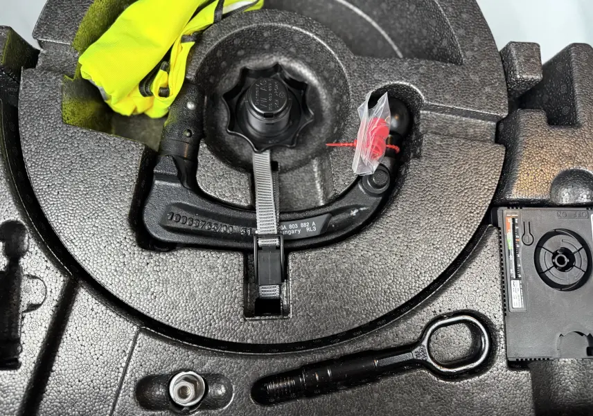 Gros plan sur le coffre à outils en mousse noire du Volkswagen T-Roc blanc, montrant le crochet de remorquage et un gilet jaune.