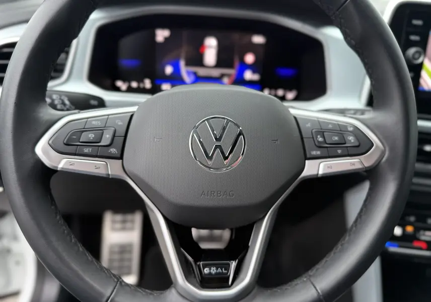Gros plan sur le volant noir du Volkswagen T-Roc 2025, avec commandes intégrées et logo VW central argenté.