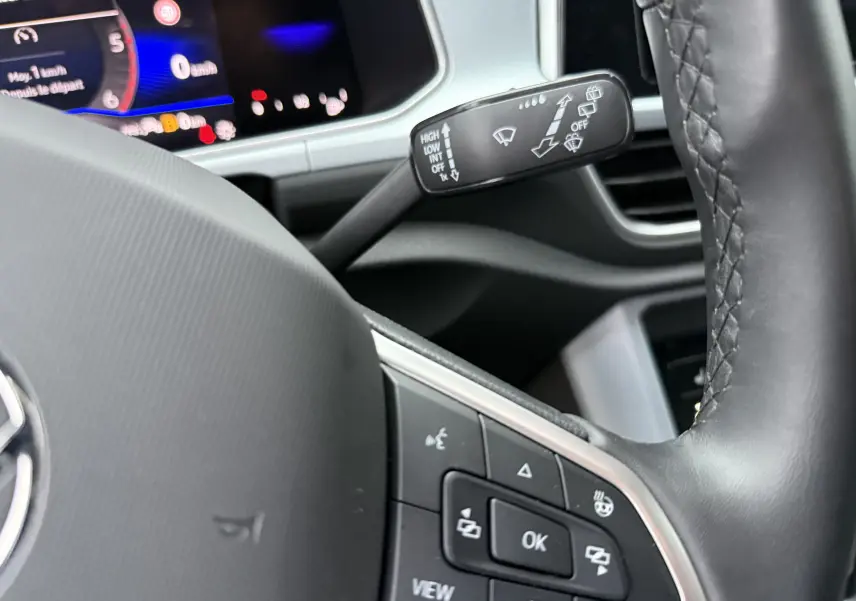 Gros plan sur le volant noir du Volkswagen T-Roc 2025 avec commandes multifonctions et tableau de bord numérique en arrière-plan.