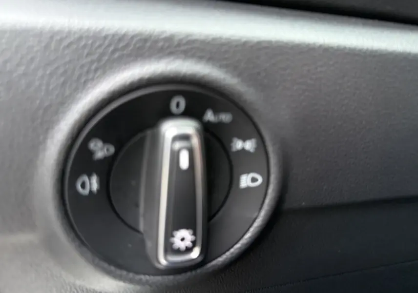 Gros plan sur le bouton de commande des phares dans l’habitacle du Volkswagen T-Roc blanc toit noir.