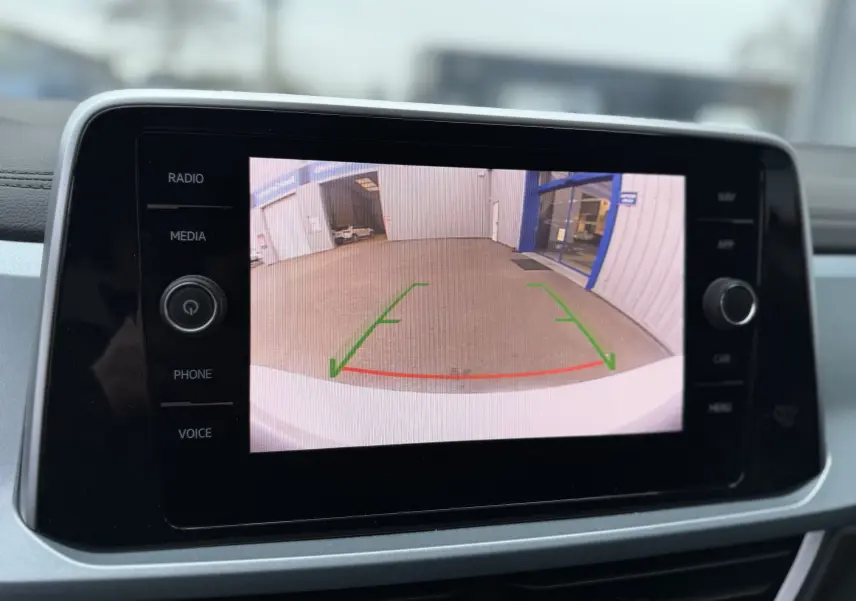 Écran central affichant la caméra de recul du Volkswagen T-Roc blanc avec toit noir, vue arrière du parking.