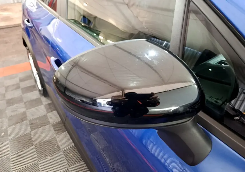 Gros plan sur le rétroviseur noir brillant côté conducteur du Renault Captur bleu, vue latérale gauche partielle.