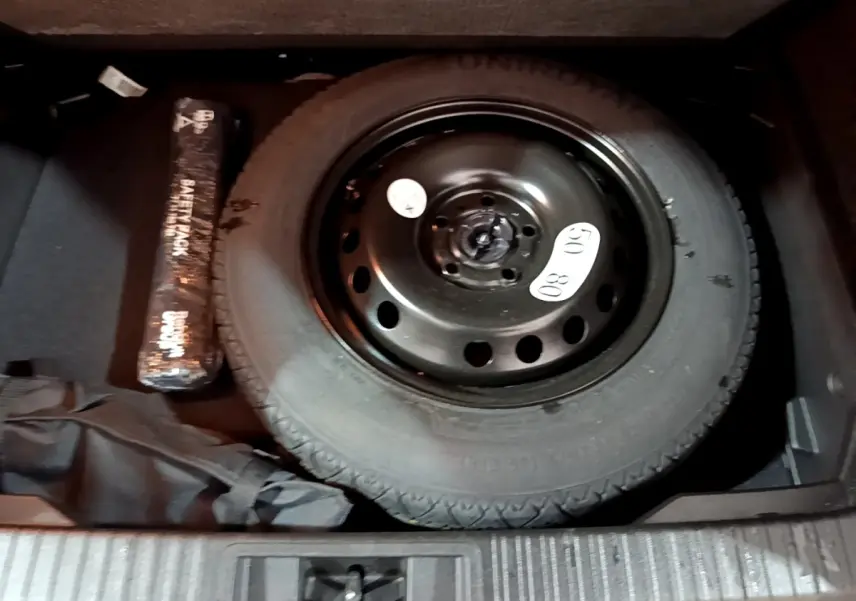 Gros plan sur la roue de secours noire dans le coffre du Renault Captur bleu, avec kit de réparation visible.