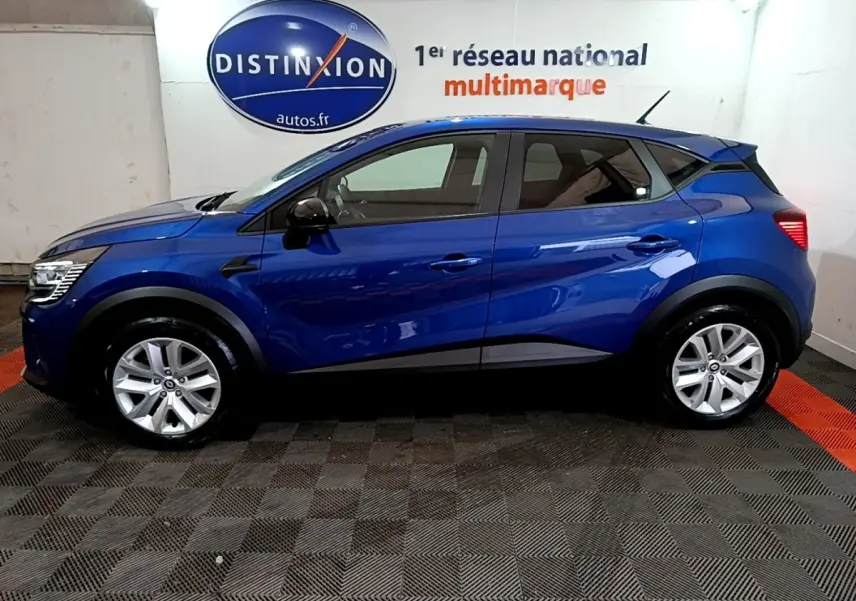 Vue de profil côté gauche d'un Renault Captur bleu 2023 avec jantes argentées, dans un showroom intérieur.