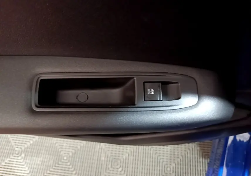 Gros plan sur le bouton de commande de la vitre électrique côté conducteur d’un Renault Captur bleu 2023.