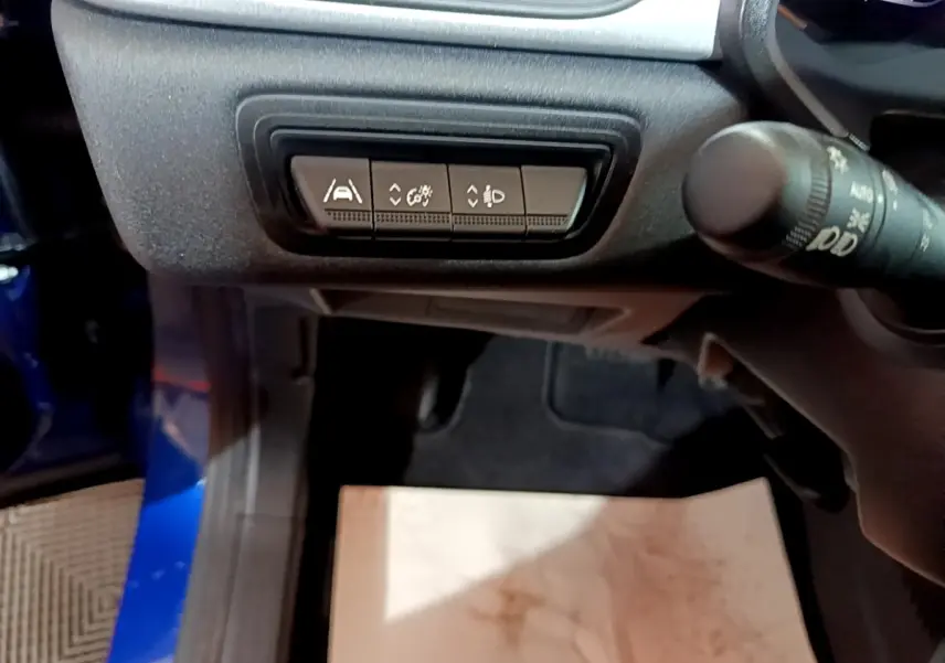 Vue intérieure côté conducteur du Renault Captur bleu, mettant en avant les boutons de réglage d'assistance et d'éclairage sous le tableau de bord.