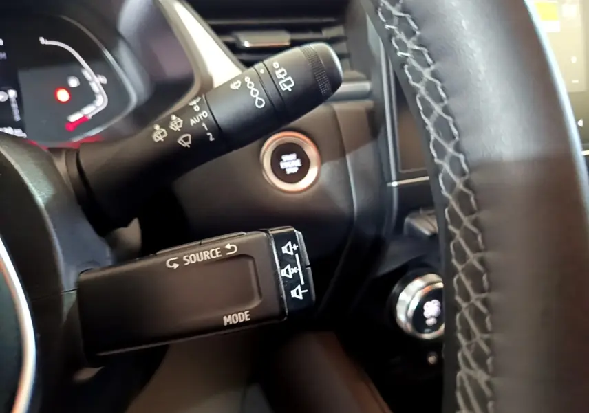 Gros plan intérieur sur le volant noir et les commandes de Renault Captur bleu, avec bouton démarrage et tableau de bord partiel.