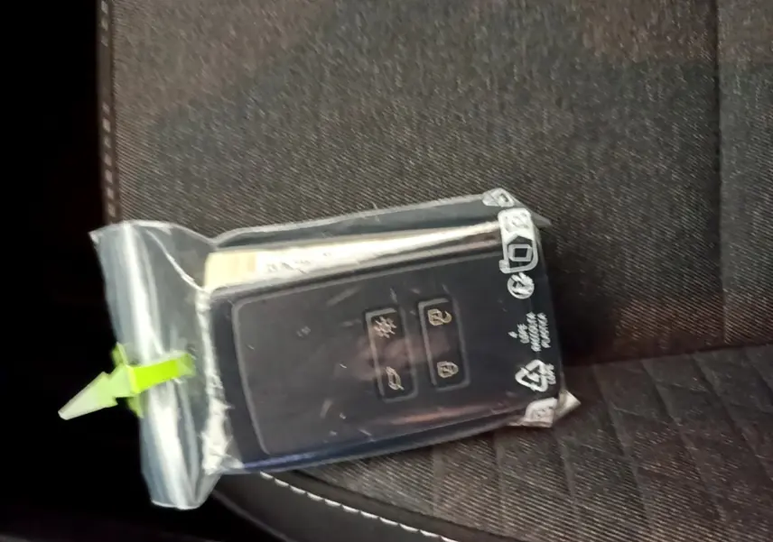 Clé Renault Captur bleu dans un sachet plastique posée sur un siège tissu noir à surpiqûres blanches.