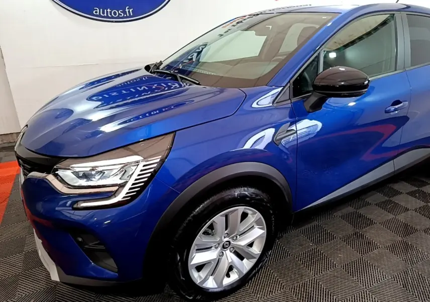Renault Captur bleu en 3/4 avant droit, avec phares LED et jantes alliage visibles sur sol intérieur.