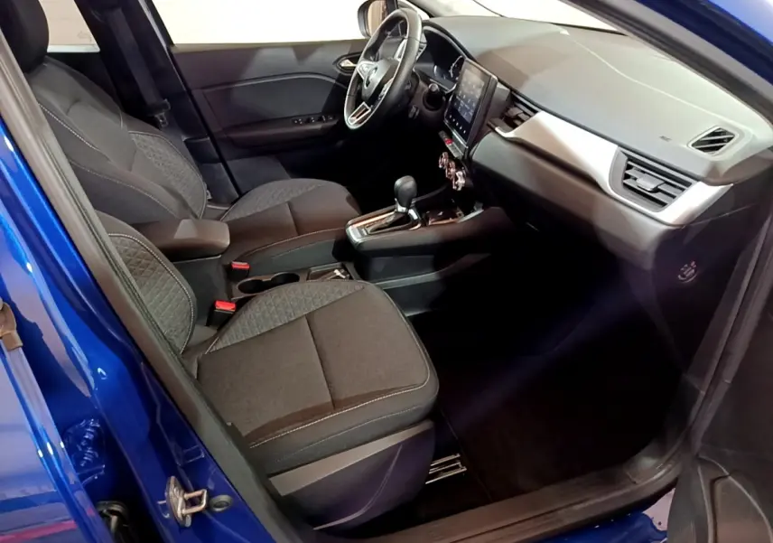 Vue intérieure côté conducteur du Renault Captur bleu 2023, avec sièges tissu noirs et tableau de bord moderne tactile.