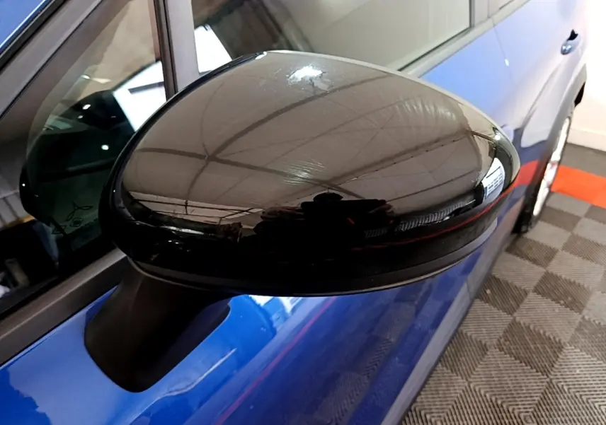 Gros plan sur le rétroviseur noir du côté gauche d'un Renault Captur bleu, avec reflet de l'environnement intérieur.