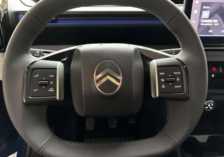 Gros plan sur le volant cuir noir de la Citroën C3 2025 avec commandes multifonctions et écran tactile en arrière-plan.
