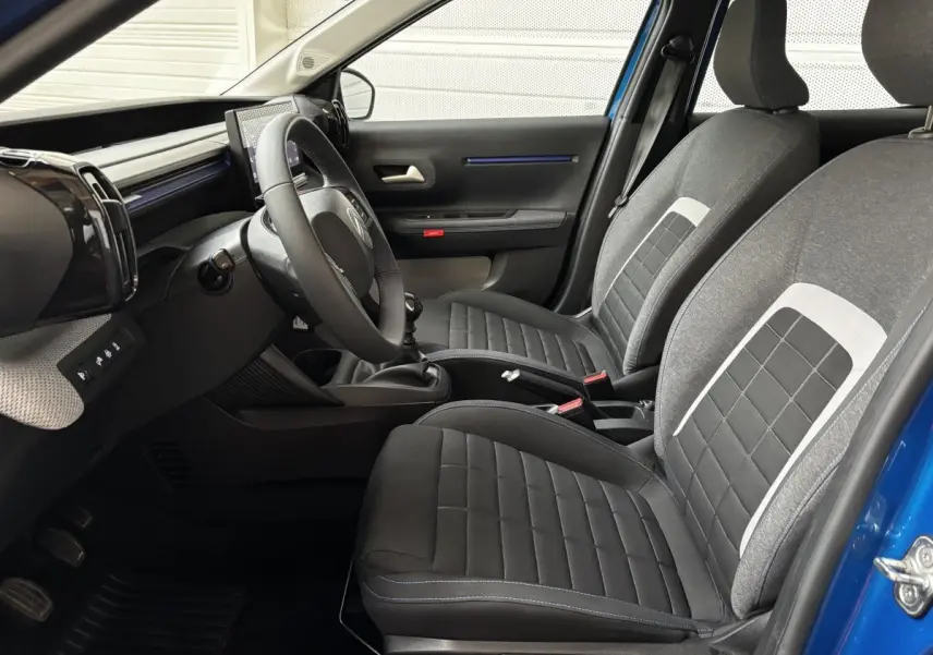 Intérieur de la Citroën C3 2025 vu côté conducteur, sièges tissu gris et noir avec surpiqûres bleues.