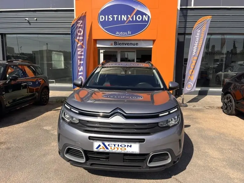 Vue avant d'un Citroën C5 Aircross gris 2019, avec calandre distinctive et toit ouvrant visible, devant un bâtiment orange.