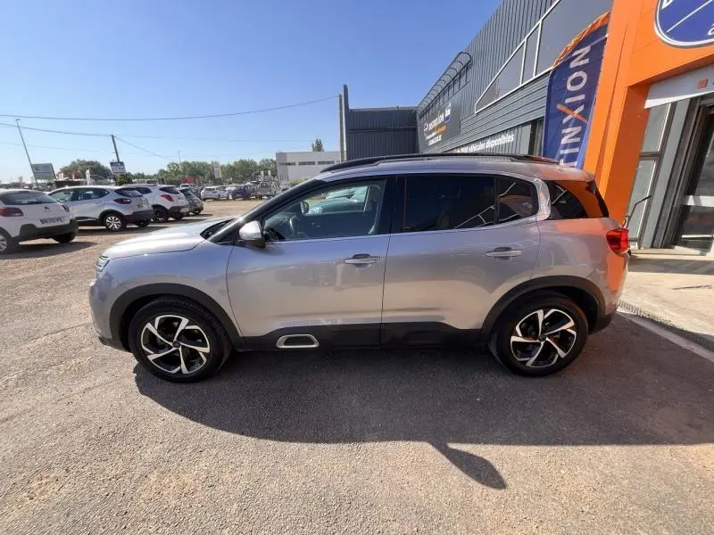 Profil droit d'un Citroën C5 Aircross gris 2019 avec jantes alliage noires et toit noir, stationné devant un bâtiment.