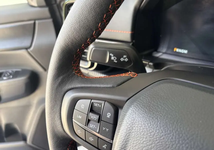 Gros plan sur le volant cuir noir avec surpiqûres rouges du Ford Ranger Wildtrak gris carbone, côté gauche intérieur.