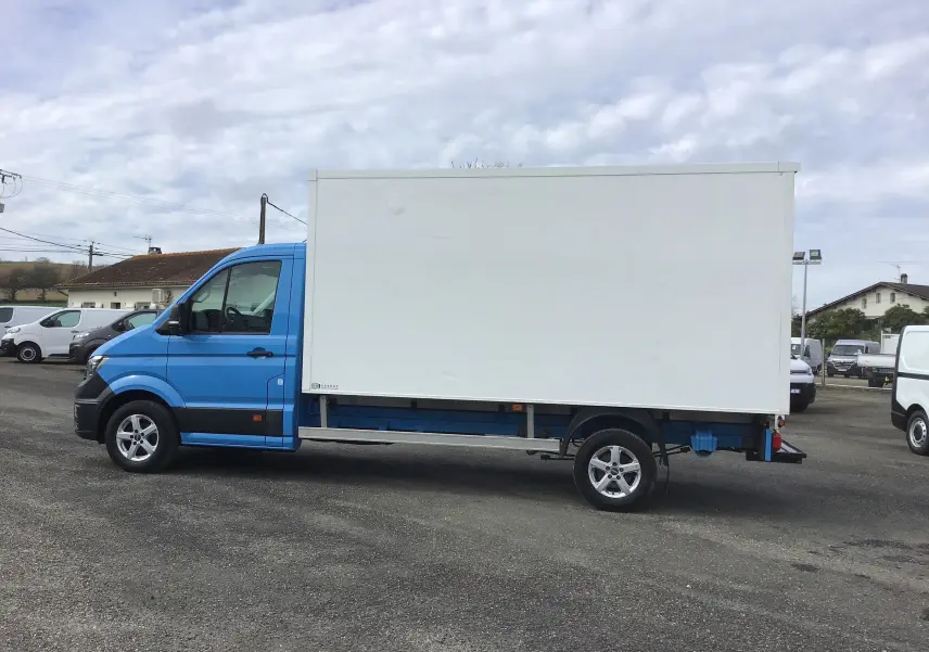 Vue de profil côté gauche d'un Volkswagen Crafter bleu avec caisse blanche de grande capacité sur un parking.