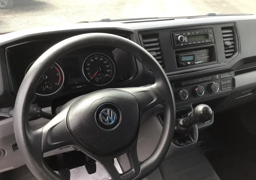 Vue intérieure du tableau de bord du Volkswagen Crafter bleu, avec volant, compteurs et levier de vitesses manuel visibles.