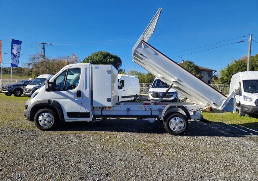 Vue de profil droit d'un FIAT Ducato Chassis Benne blanc 2023 avec benne acier relevée et coffre latéral fermé.