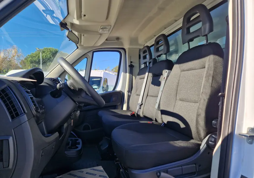 Intérieur du FIAT Ducato Chassis Benne blanc 2023, vue côté conducteur sur les trois sièges avant en tissu noir.