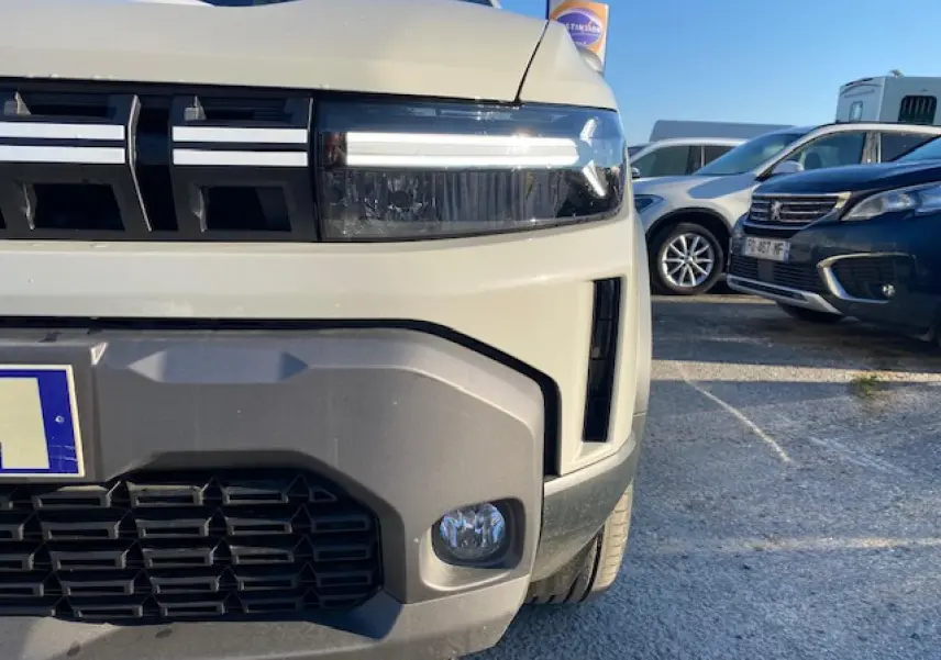 Gros plan sur l'avant droit du Dacia Duster beige Sandstone 2025, mettant en valeur ses phares LED et sa calandre noire.