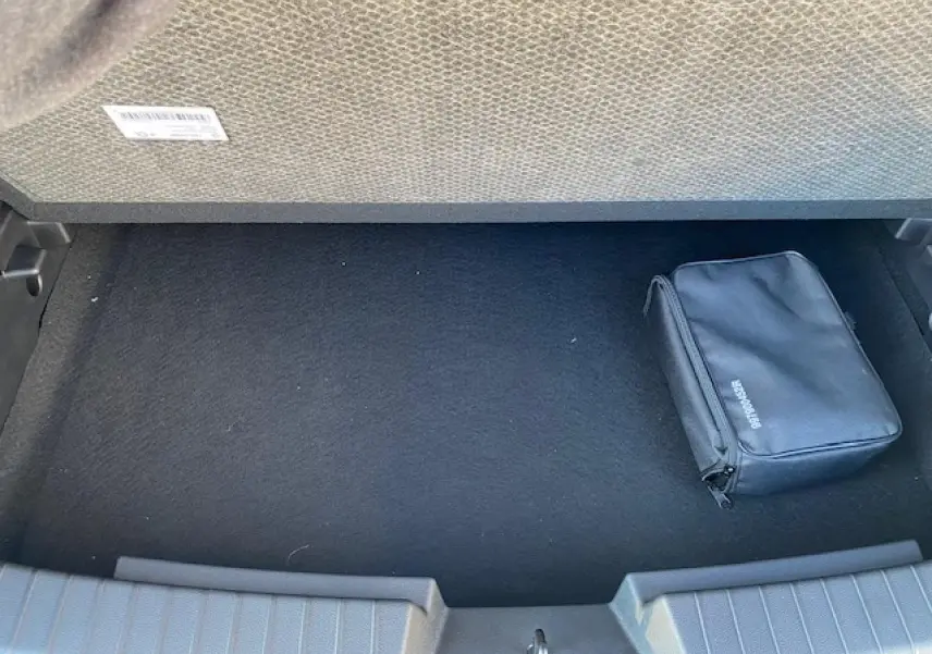Coffre ouvert d'un Dacia Duster 2025 beige Sandstone, vue intérieure avec un sac noir de secours posé à droite.