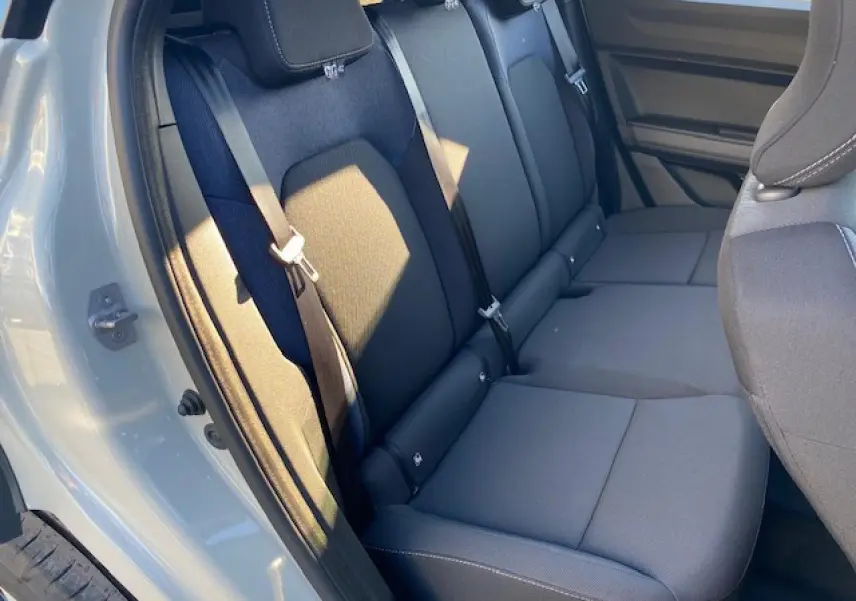 Vue intérieure sur les sièges arrière noirs du Dacia Duster 2025, porte arrière beige sandstone ouverte côté gauche.