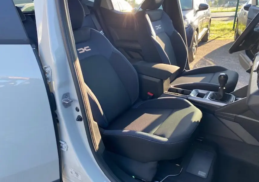 Vue intérieure côté conducteur du Dacia Duster 2025 avec sièges noirs et levier de vitesse manuel visible.