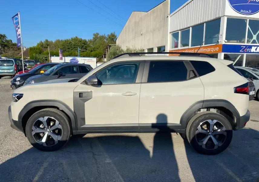 Profil côté gauche du SUV Dacia Duster 2025 beige Sandstone avec jantes noires et détails noirs contrastants.