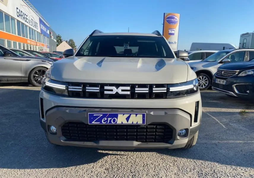 Vue frontale du Dacia Duster 2025 beige Sandstone avec calandre noire et plaque d'immatriculation Zero KM visible.