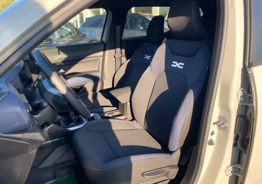 Intérieur du Dacia Duster 2025 beige Sandstone, vue côté conducteur sur les sièges sport noirs avec logo DC brodé.