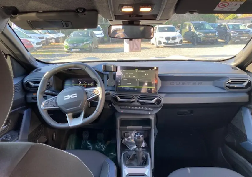Vue intérieure avant du Dacia Duster 2025 beige sandstone, avec tableau de bord moderne et boîte manuelle visible.