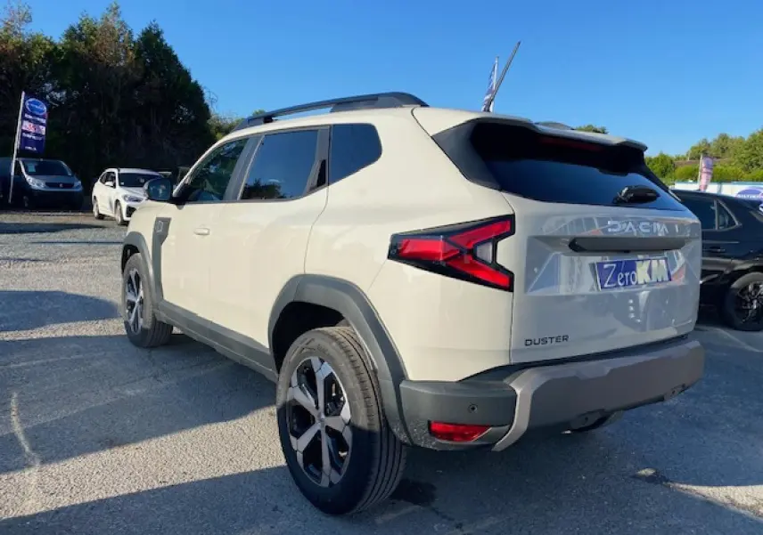 Dacia Duster 2025 beige Sandstone vu en 3/4 arrière droit, avec feux arrière en forme de flèche et jantes noires.