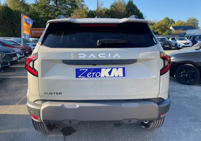 Vue arrière du Dacia Duster 2025 beige Sandstone avec feux arrière en forme de C et plaque Zéro KM visible.