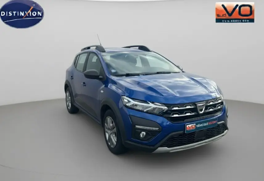 Dacia Sandero Stepway bleu foncé vue 3/4 avant droit avec barres de toit et feux allumés sur fond neutre.