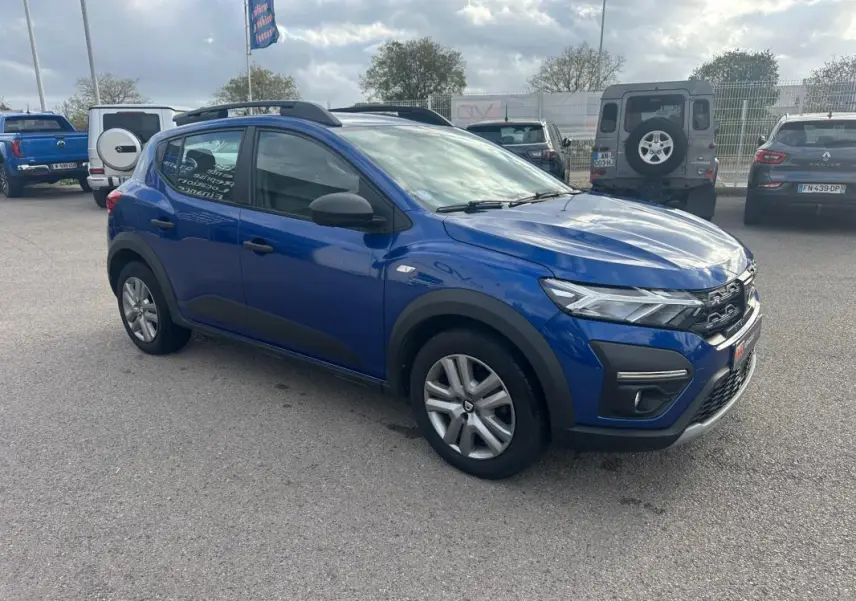 Dacia Sandero Stepway bleu foncé vue 3/4 avant droit avec barres de toit et vitres surteintées.