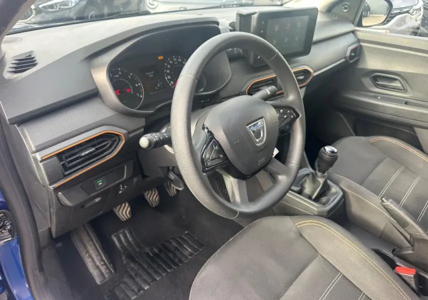 Intérieur de la Dacia Sandero bleu foncé 2021, vue côté conducteur avec volant, tableau de bord et boîte manuelle visibles.